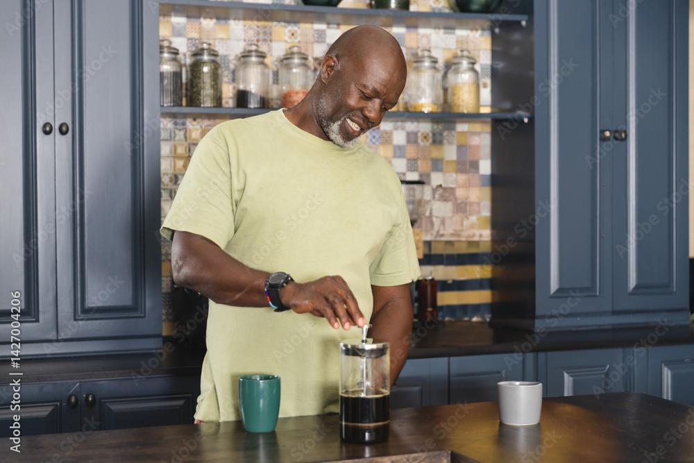 Senior African American man pressing down French press on kitchen island, with green and white mugs