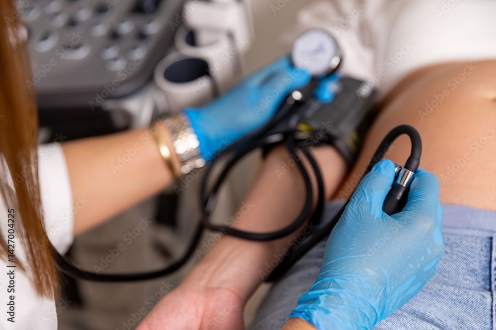 Close up female doctor measures the blood pressure of a pregnant woman lying on a couch in a clinic. Selective focus. Top view