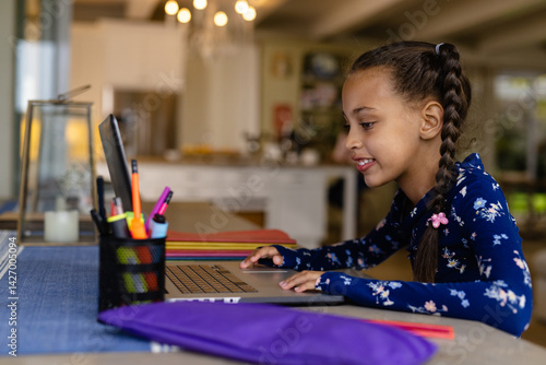 Obraz na płótnie Child girl sitting at table using laptop in home kitchen, with pen holder, notebooks, copy space w salonie