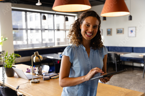 Female office professional using tablet in modern co-working space, with laptop desk lamp and plant