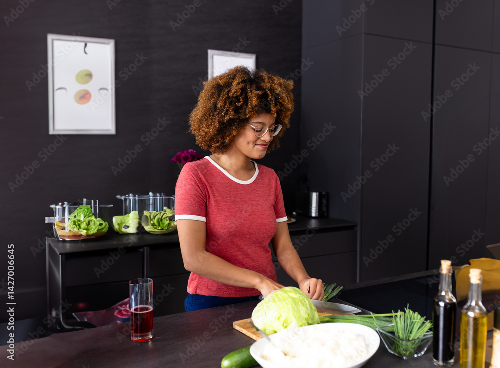 Diverse woman slicing cabbage on cutting board at modern kitchen island, with chopped vegetables