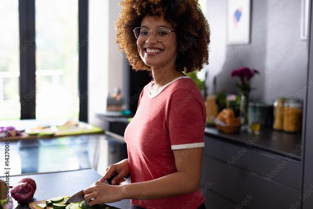 Woman smiling while slicing cucumbers in modern kitchen, with wooden cutting board and chef's knife