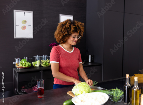 Diverse woman slicing cabbage on cutting board at modern kitchen island, with chopped vegetables