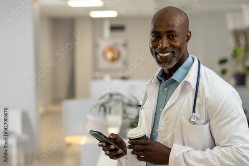 Obraz na płótnie African American male doctor smiling, holding smartphone and coffee cup in clinic, copy space w salonie