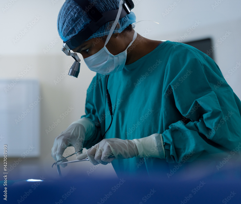 African American female surgeon leaning over patient in surgery room holding forceps and retractor