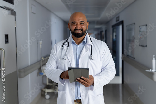 Obraz na płótnie Male doctor holding tablet and smiling in hospital corridor, with stethoscope and IV stand w salonie