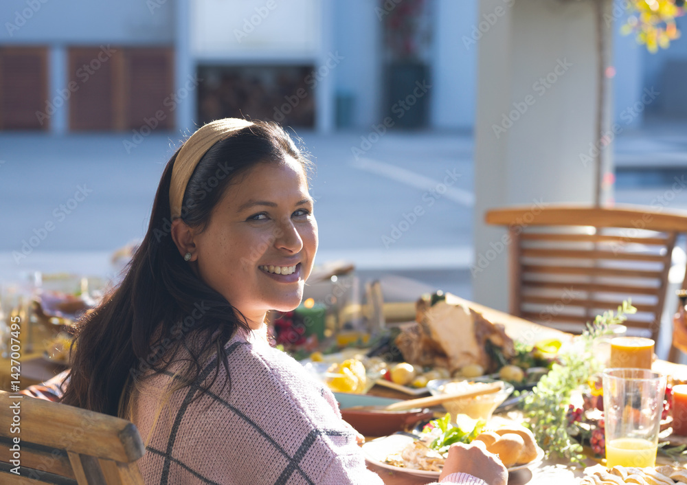 Woman turning and smiling toward camera at outdoor patio table, with roasted turkey and bread rolls