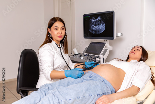 Obraz na płótnie Female doctor with stethoscope listening to pregnant woman's belly on sofa in clinic and measuring the blood pressure. Maternity, pregnancy, fertility concept. Embryo check in. High quality photo. w salonie