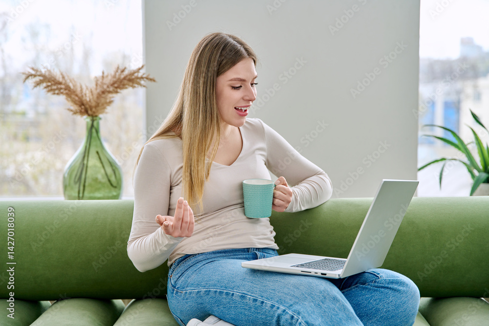 Young woman using laptop for video chat sitting on sofa at home
