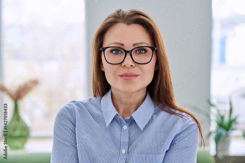 Headshot portrait of serious middle aged businesswoman with glasses in blue shirt