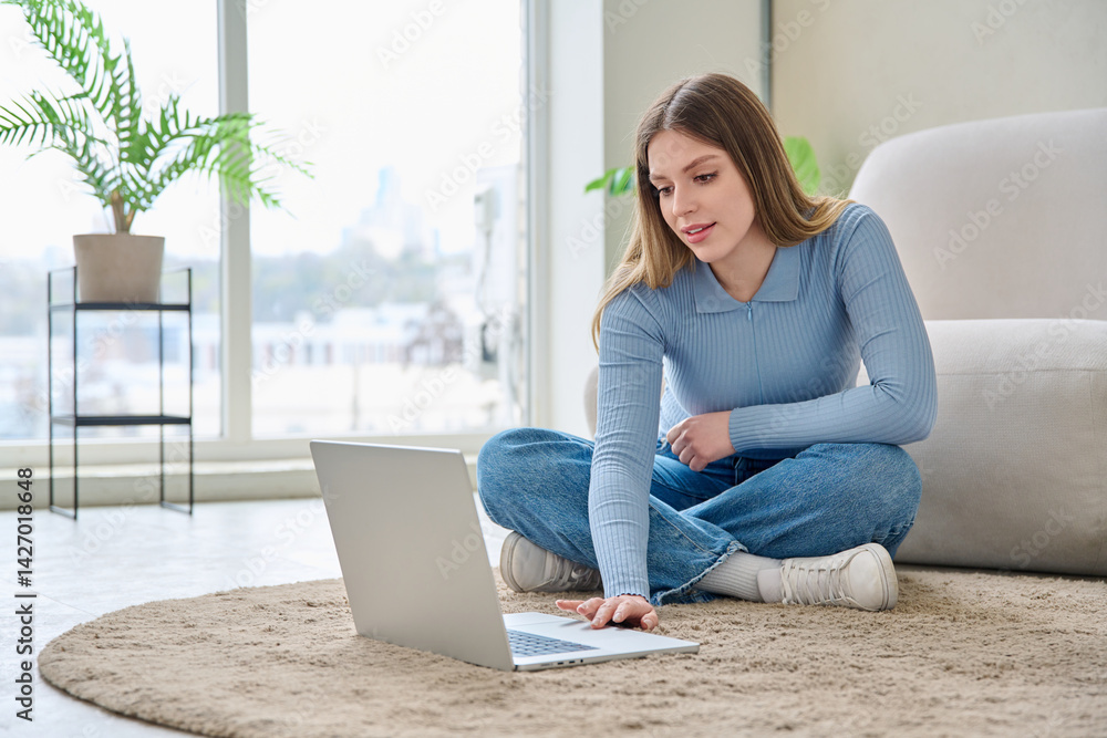 Young woman using laptop, sitting on floor at home