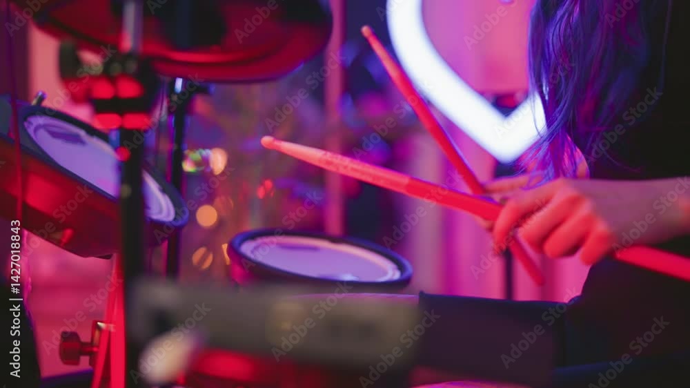 Partial view of lady with long wavy hair covering her face while playing electronic drum set in ambient studio featuring soft neon heart ring light and purple pink background with blurred glow Partial view of lady with long wavy hair covering her face while playing electronic drum set in ambient studio featuring soft neon heart ring light and purple pink background with blurred glow