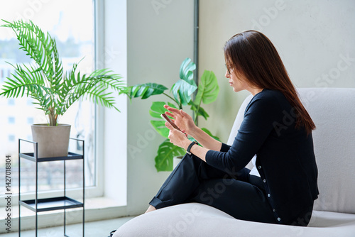 Obraz na płótnie Anxious nervous middle aged woman looking at smartphone sitting on sofa w salonie