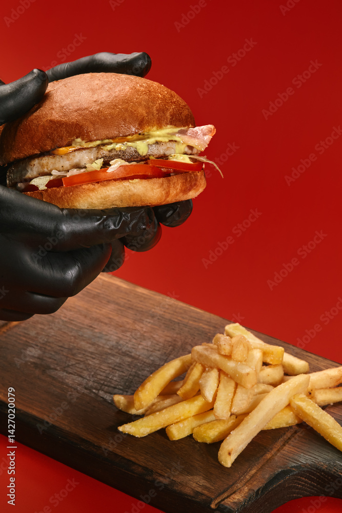 Chef holding tasty burger with french fries on red background