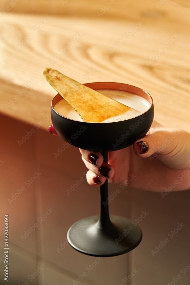 Woman holding a coupe glass with a cocktail and a garnish