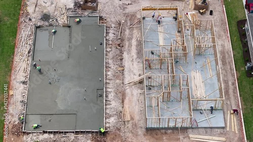 Aerial view of newly poured concrete slab next to home that is being constructed with wooden framework in Georgetown Texas