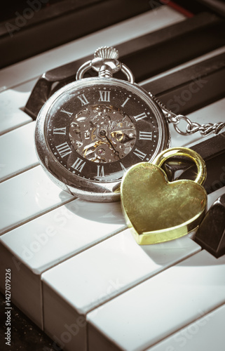Obraz na płótnie A retro pocket watch or Antique pocket watch with Golden heart shaped love padlock on Piano keys background in Vintage tone. The concept of the time of love, use it as your Wallpaper, Poster and Space w salonie