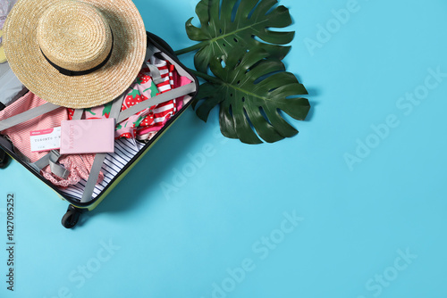 Obraz na płótnie Open suitcase with different clothes, hat and passport on light blue background, flat lay. Space for text w salonie