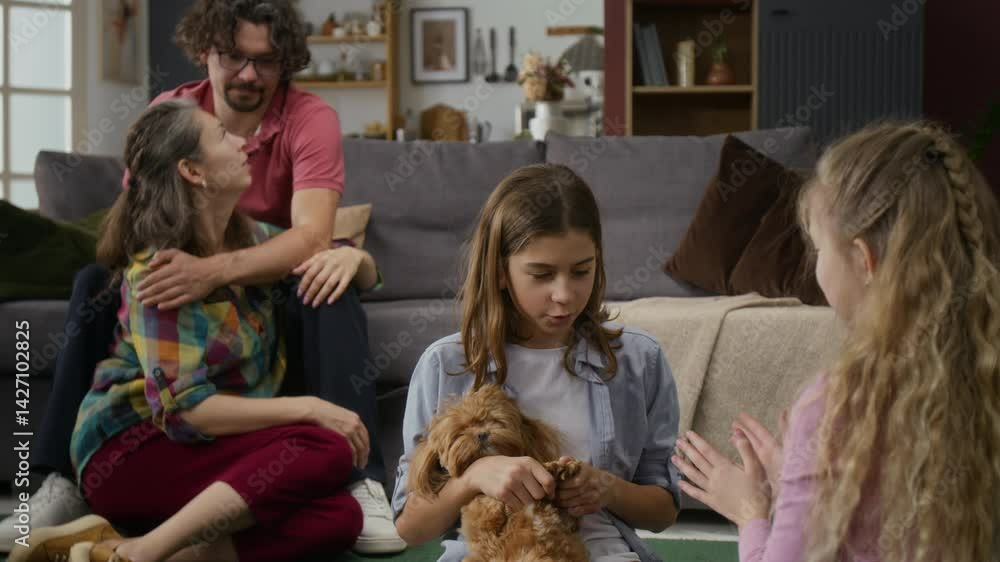 Medium full shot of happy Caucasian family relaxing together at home – boy and girl playing clapping game with pet dog, while husband with disability and wife are hugging and chatting Medium full shot of happy Caucasian family relaxing together at home – boy and girl playing clapping game with pet dog, while husband with disability and wife are hugging and chatting