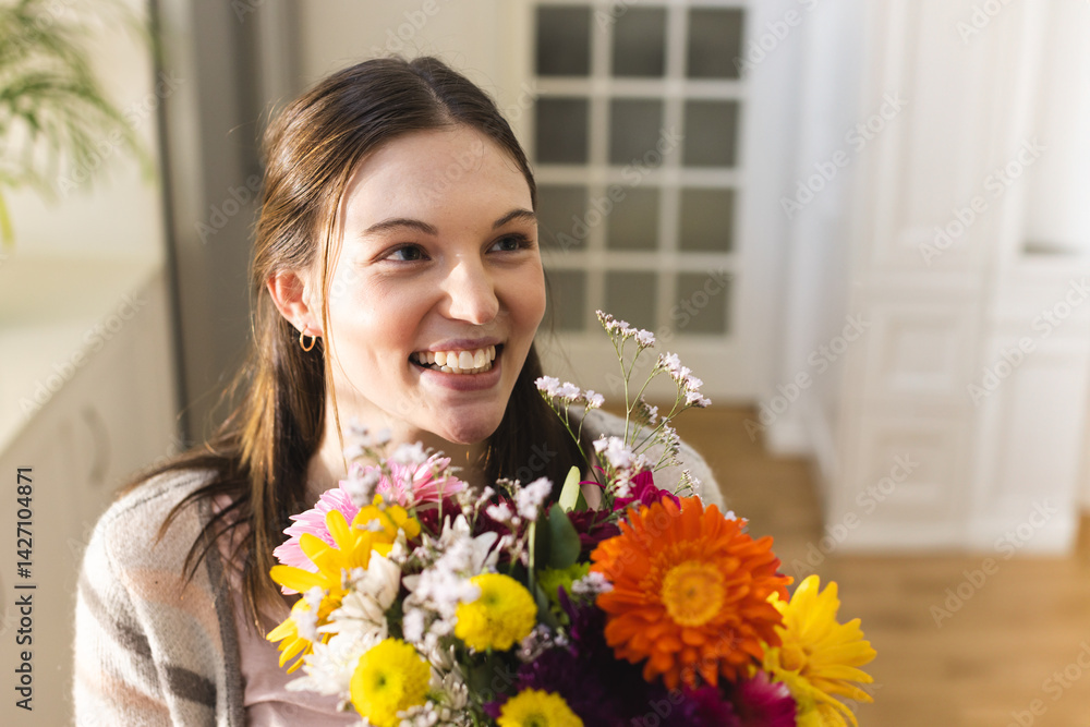 Woman smiling and holding colorful bouquet in home hallway, with built-in cabinet and plant