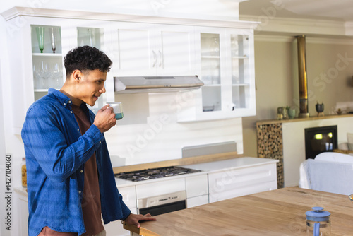 Man holding ceramic mug in modern kitchen with wooden island, gas stove, blue teapot, copy space