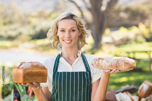 woman holding sandwich loaf and baguette at outdoor farmers market stall, showing fresh produce