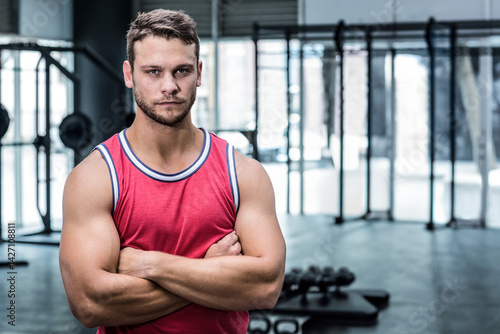 Obraz na płótnie Muscular man standing with arms crossed in modern gym, with dumbbell rack and weight bench w salonie