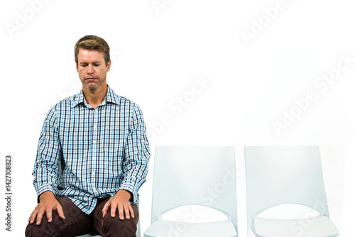 Man sitting among empty chairs in clean studio, wearing checkered shirt and brown pants, copy space