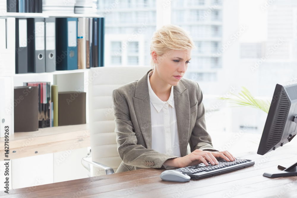 bi-racial woman typing on keyboard at office desk with computer monitor, plant