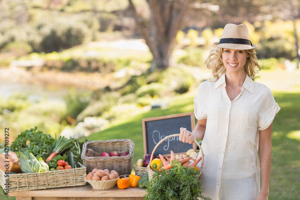 Woman displaying wicker basket of organic produce at table by pond with chalkboard sign, copy space