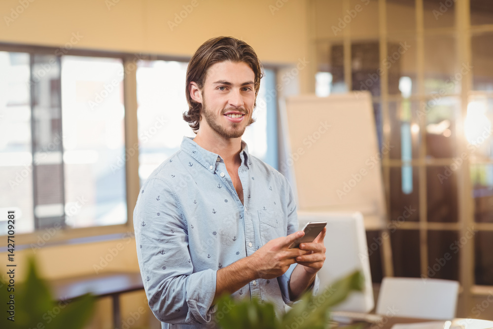 Man standing holding smartphone in office space, with flip chart and computer monitor