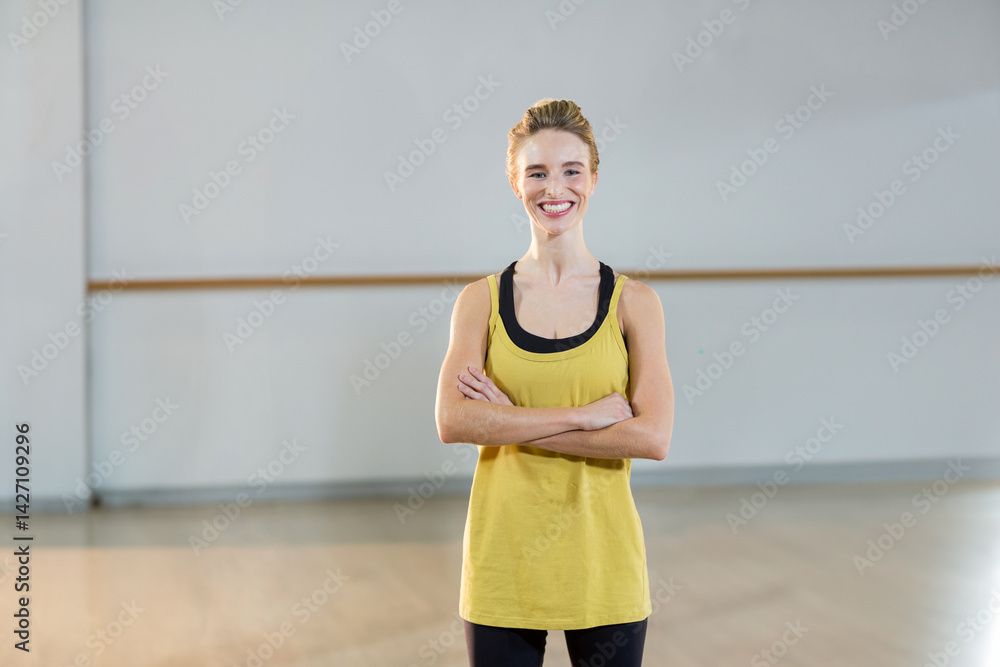 Young woman smiling and standing with crossed arms in dance studio, with ballet barre