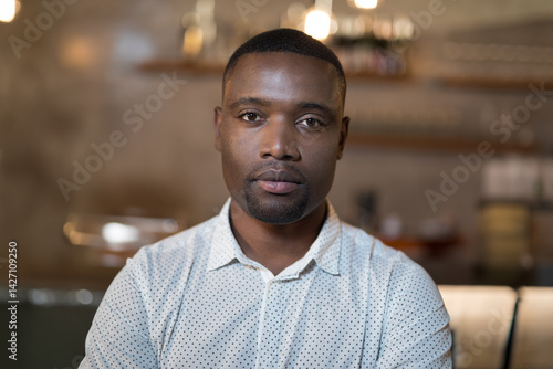 Obraz na płótnie Young African American man looking into camera at cafe counter, with pastry stand, warm lights w salonie