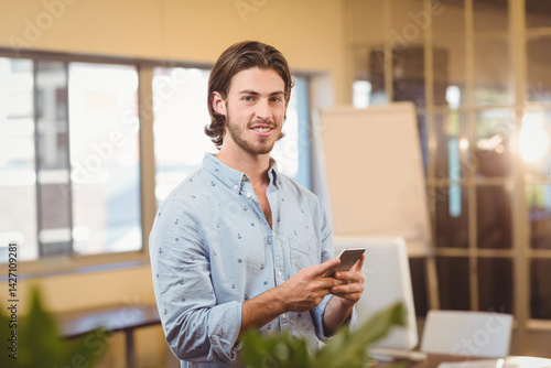 Man standing holding smartphone in office space, with flip chart and computer monitor