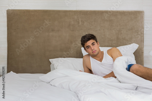 Obraz na płótnie Man reclining on bed in bedroom, with rumpled white bedding and beige headboard, copy space w salonie