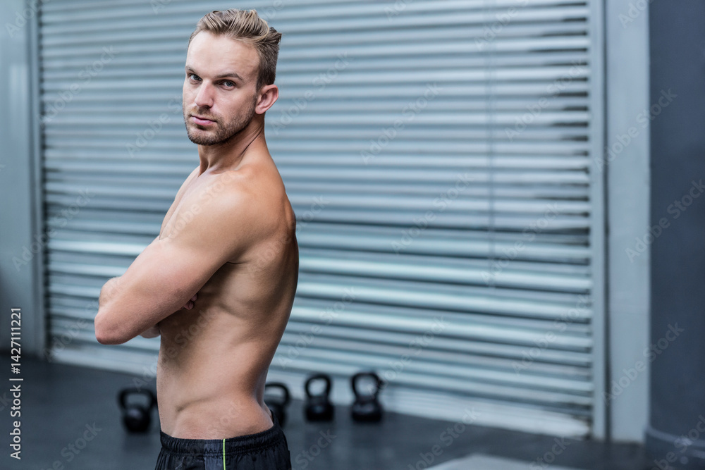Fototapeta premium Man standing with crossed arms in fitness studio, showing kettlebells, copy space