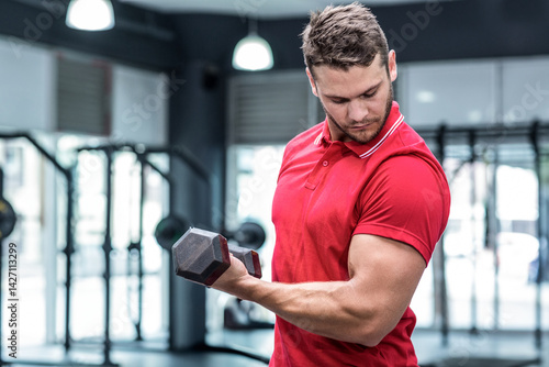 Obraz na płótnie Young adult man curling hex dumbbell in modern gym with weight racks, focusing on strength w salonie