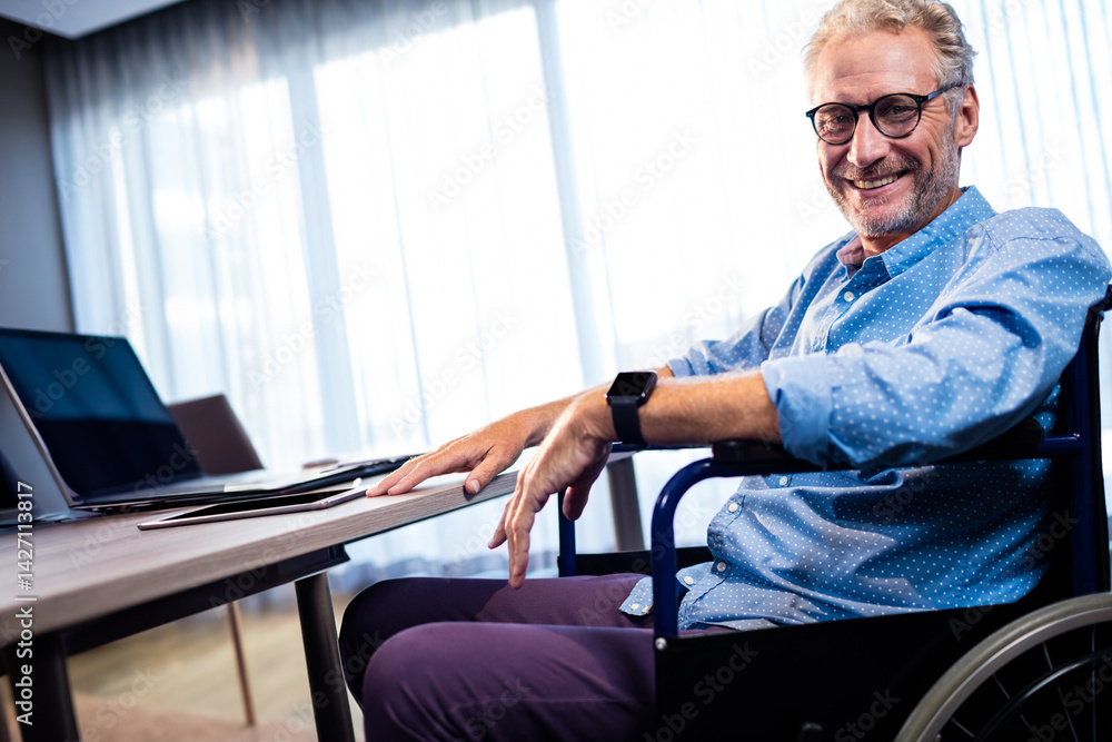 Man working at desk in office from wheelchair, using laptop smartphone and smartwatch, copy space