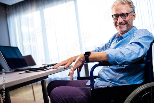 Obraz na płótnie Man working at desk in office from wheelchair, using laptop smartphone and smartwatch, copy space w salonie