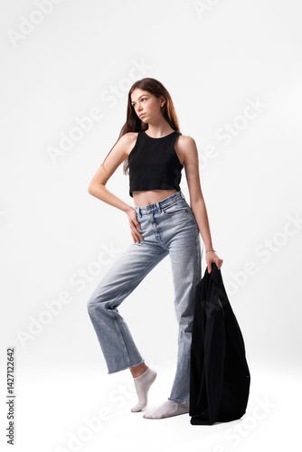 Model posing in casual outfit with black top and denim jeans in a minimalist studio setting during a fashion photoshoot