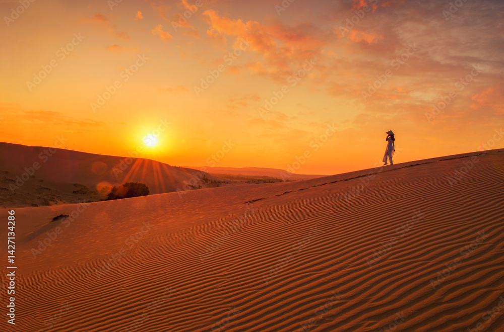 Side view of a Woman in a traditional Ao Dai dress and non la hat walking in the Mui Ne Sand Dunes at sunset, Mui Ne, Phan Thiet, Vietnam Side view of a Woman in a traditional Ao Dai dress and non la hat walking in the Mui Ne Sand Dunes at sunset, Mui Ne, Phan Thiet, Vietnam
