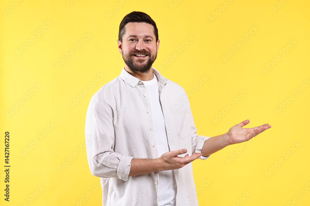 Happy man welcoming friends or guests on yellow background Happy man welcoming friends or guests on yellow background