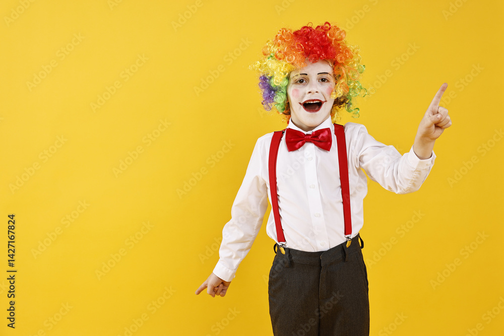 Emotional little boy dressed like clown pointing upwards on yellow background, space for text. Surprise party Emotional little boy dressed like clown pointing upwards on yellow background, space for text. Surprise party