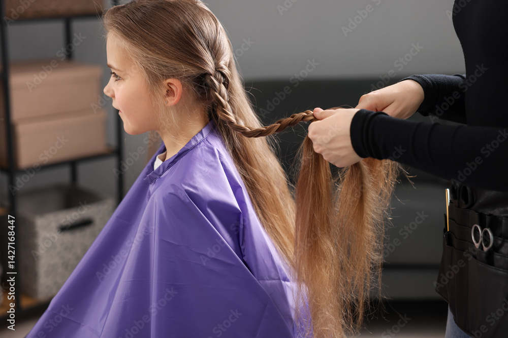 Fototapeta premium Hairstylist braiding girl's hair in salon, closeup