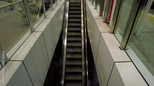 Overhead view of an escalator in a modern building.  Clean lines, glass walls, and neutral colors.