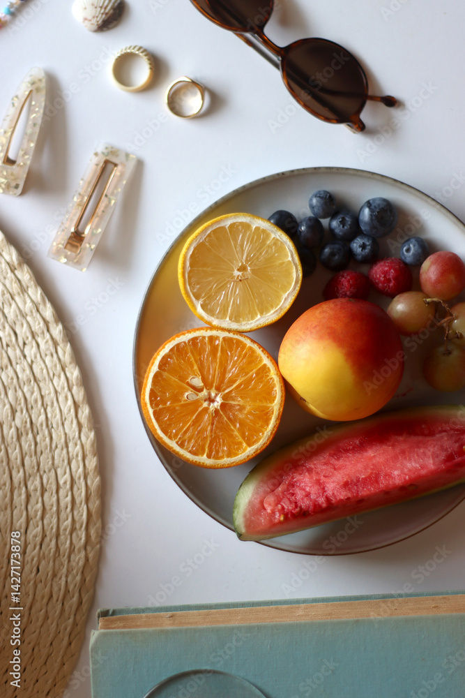 Glass of cocktail, straw hat, sunglasses, books, fresh fruit, chocolate and accessories. Summer essentials on the table. Top view.