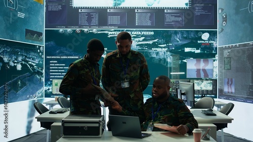Obraz na płótnie In a high tech military office, soldiers team analyze real time data collected by surveillance system. Staff interpret intelligence and coordinate operations to ensure national defense. Camera B. w salonie