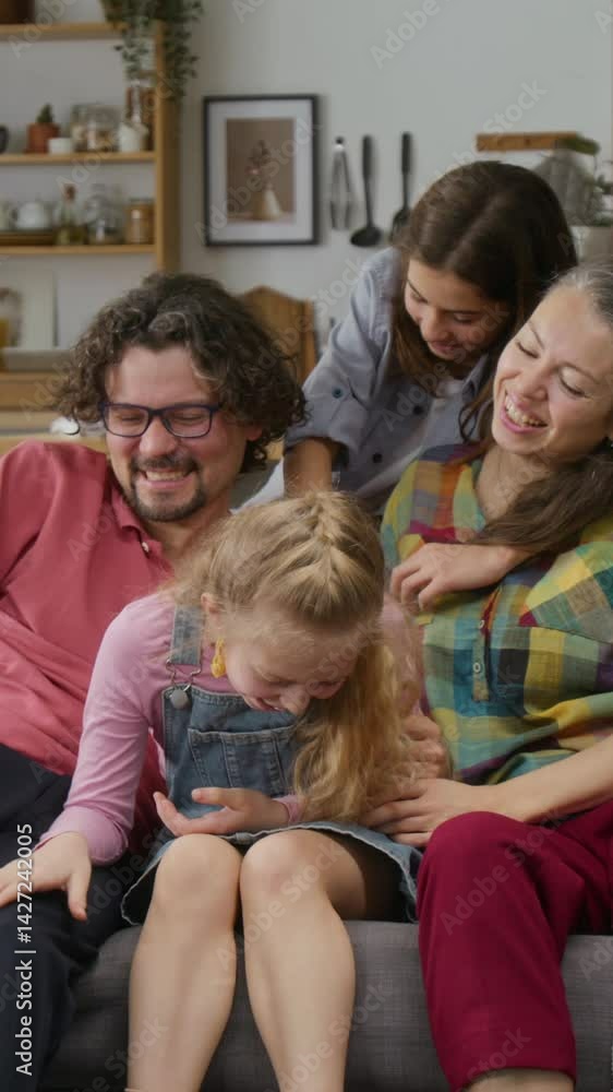 Medium vertical shot of Caucasian father with missing arm disability, happy mother, teenage son and young daughter sitting on couch, cuddling, playing tickling game and laughing with joy Medium vertical shot of Caucasian father with missing arm disability, happy mother, teenage son and young daughter sitting on couch, cuddling, playing tickling game and laughing with joy