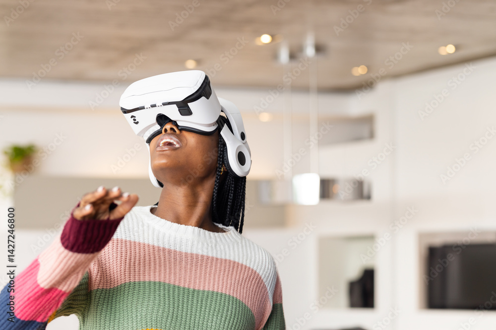 Young African American woman experiencing virtual reality in living room, wearing VR headset Young African American woman experiencing virtual reality in living room, wearing VR headset