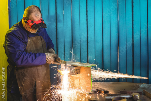 Man operating cutting torch on metal workbench in workshop, with sparks flying, copy space